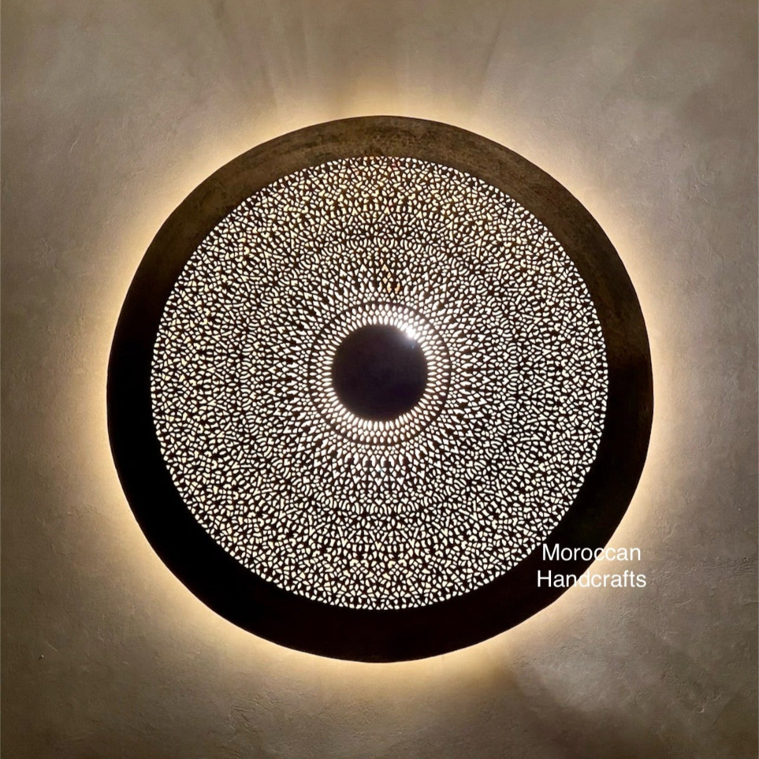 Ambient interior shot of a large round Moroccan lantern creating a warm, cozy light effect on a textured wall.