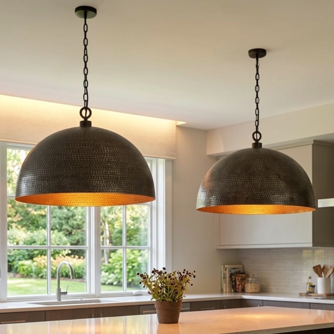 Hand-hammered brass dome pendant lights with warm interior finish installed over a white marble kitchen island in a brightly lit modern home