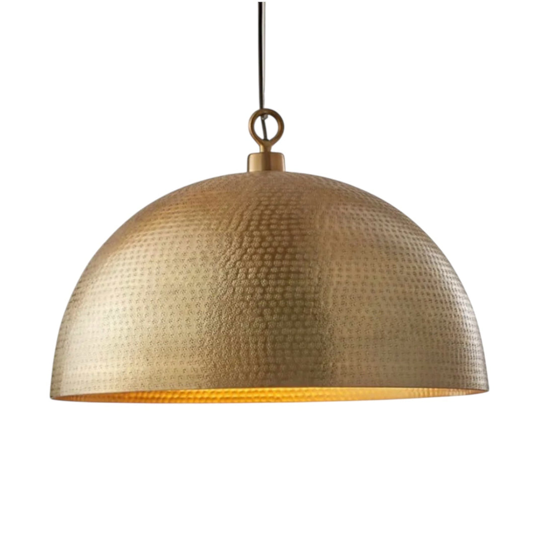 Three brass hammered dome lights suspended over a dark marble bar counter with liquor bottles and a blurred city skyline at dusk.