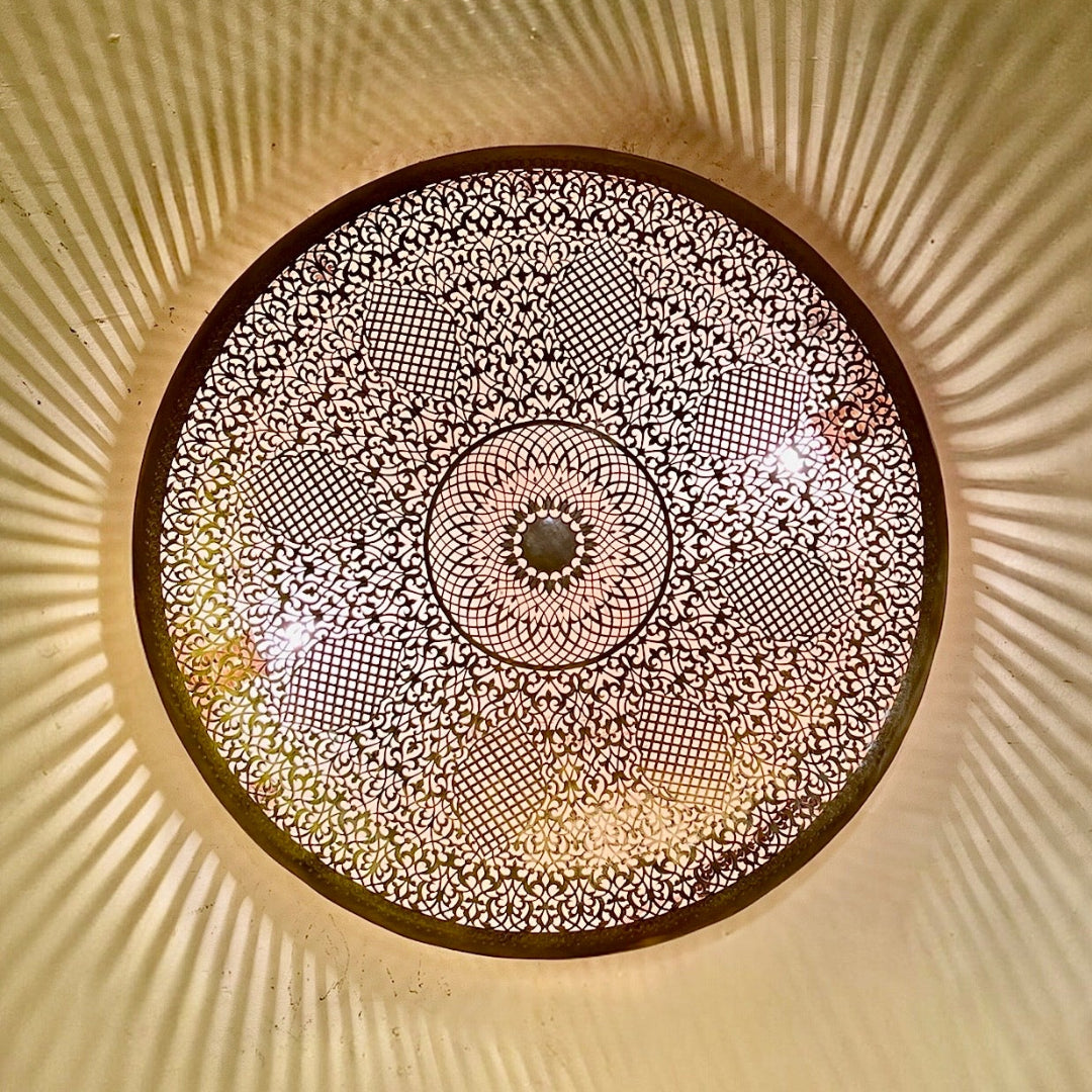 Warm ambient light glowing through a detailed, hand-carved Moroccan brass sconce.