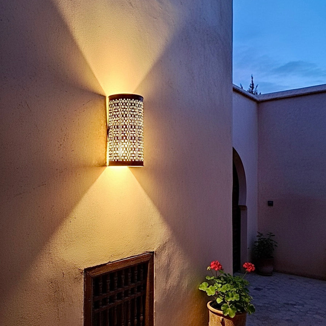 Warm light effect from a Moroccan brass wall sconce, highlighting the complex handmade -cut patterns on the wall.