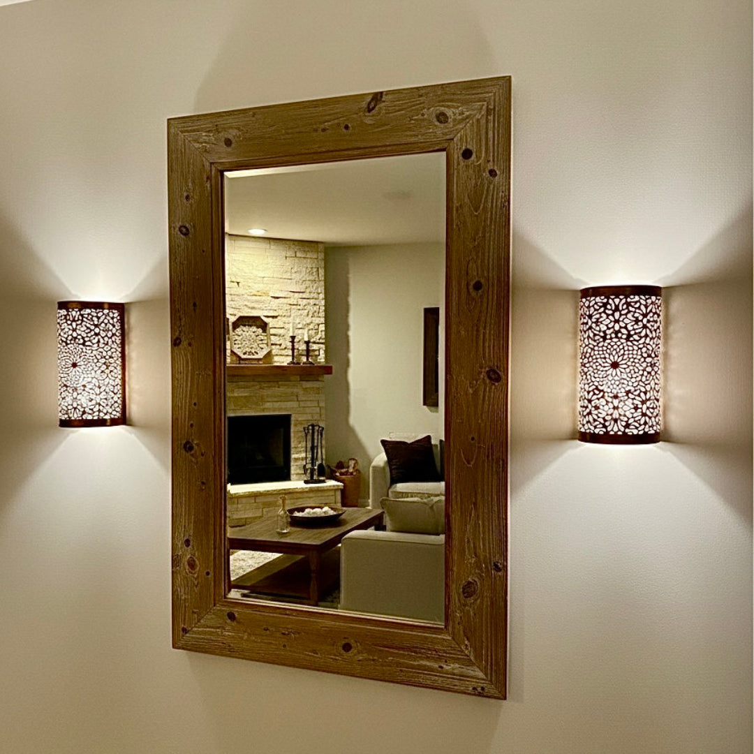 A rustic wooden framed mirror flanked by two ornate brass wall sconces, showcasing a blend of traditional Moroccan craftsmanship and modern interior design.