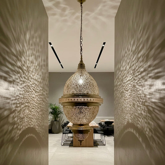 Authentic Moroccan brass chandelier hanging in a luxury high-ceiling hallway with classical architecture.