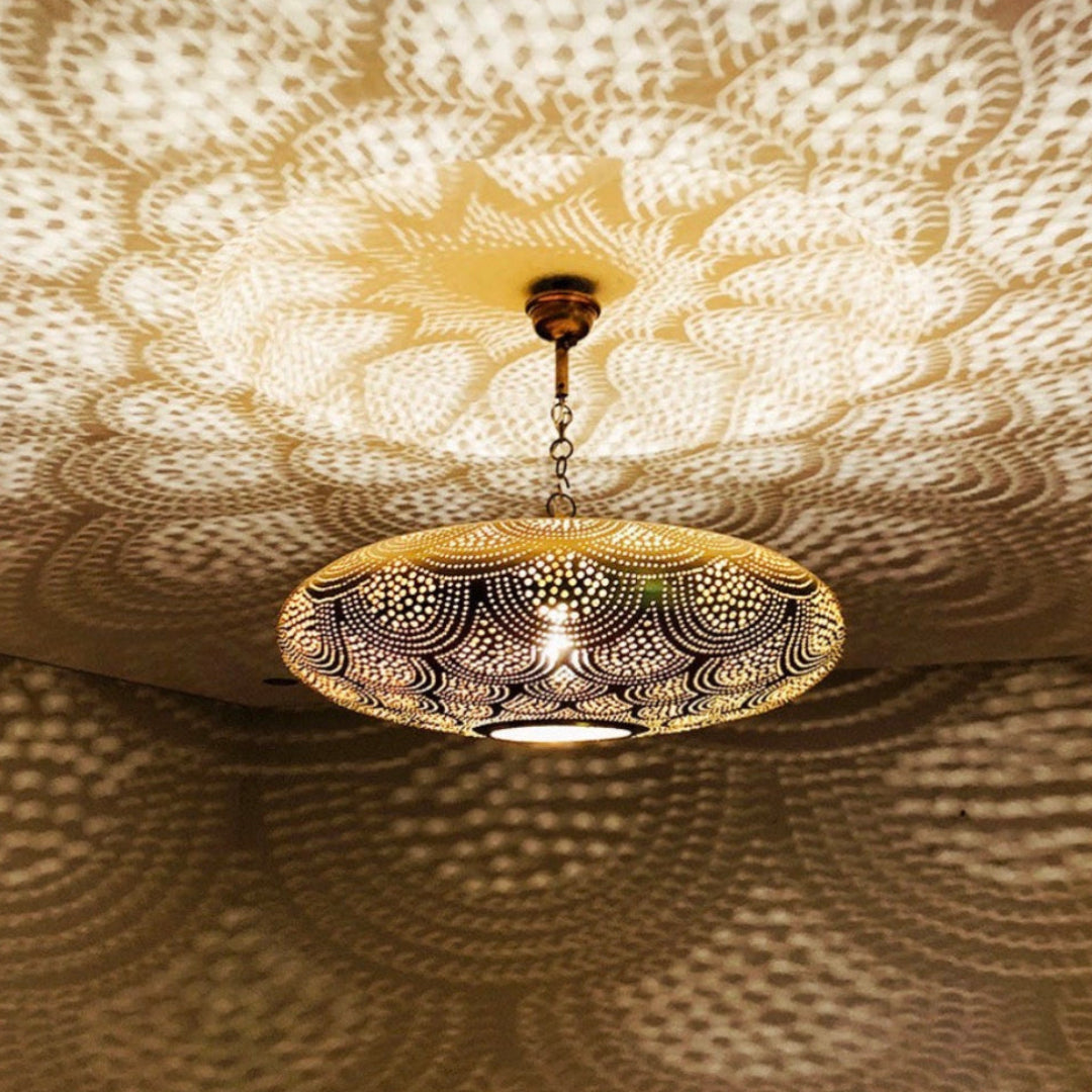 Moroccan brass hanging lamp glowing in the dark, projecting geometric shadows on white walls.