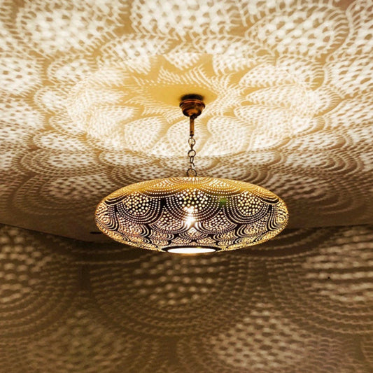 Moroccan brass hanging lamp glowing in the dark, projecting geometric shadows on white walls.