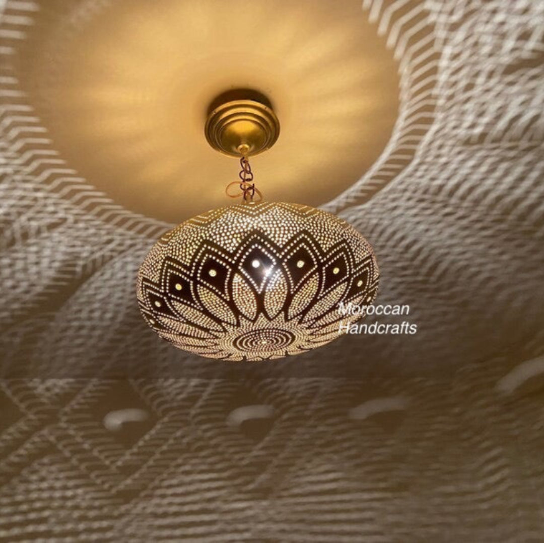 Handcrafted circular brass Moroccan wall sconce with intricate geometric piercing, casting a dramatic starburst light pattern on a textured wall.