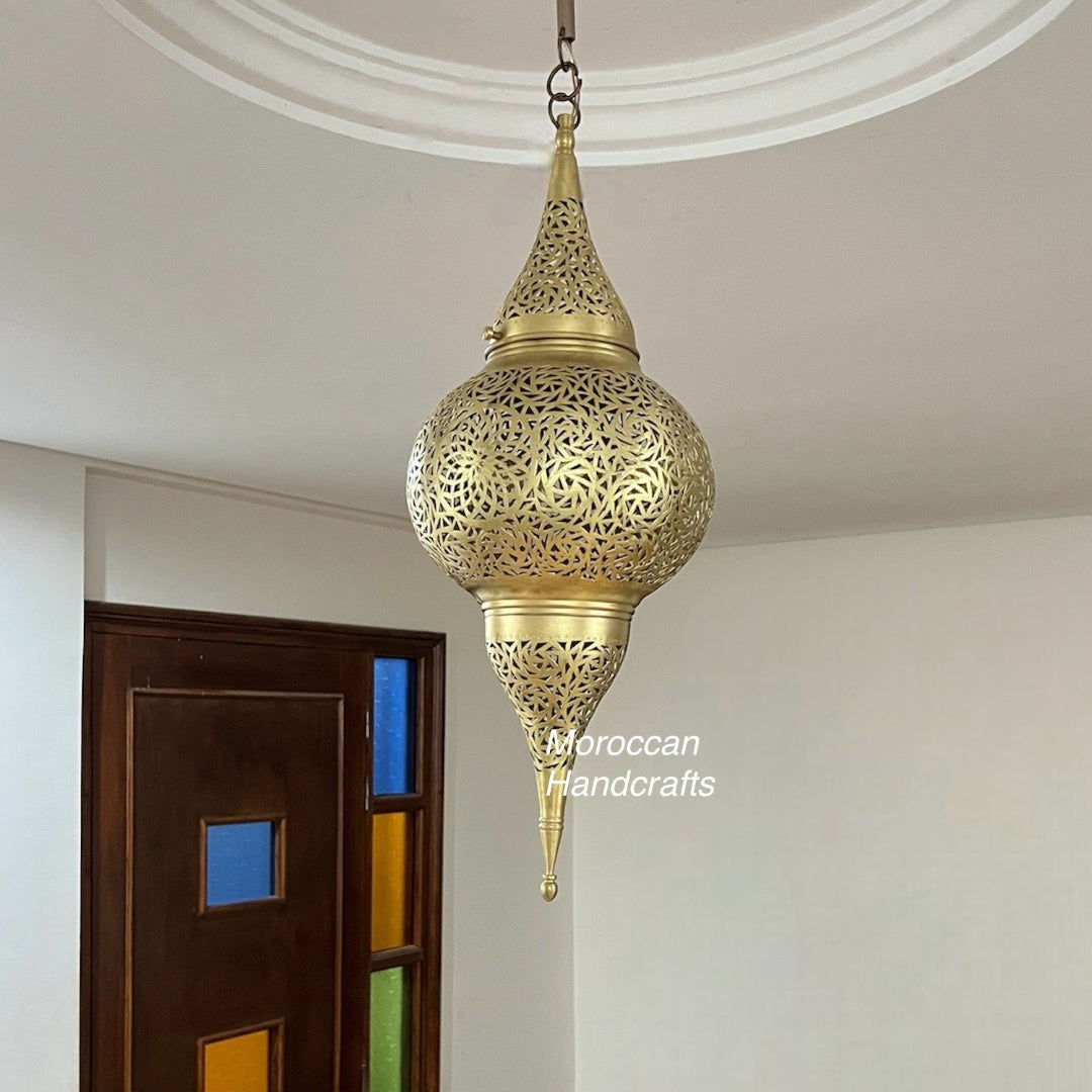 Hand-pierced brass Moroccan pendant lamp hanging from a white ceiling, casting dramatic, swirling shadow patterns across the walls.