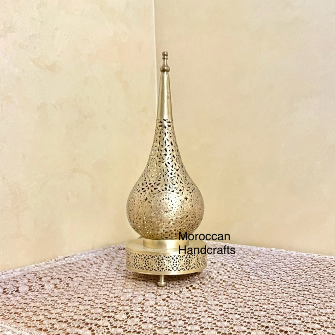 Moroccan brass lamp standing on a lace tablecloth, showing the teardrop shape and golden finish.