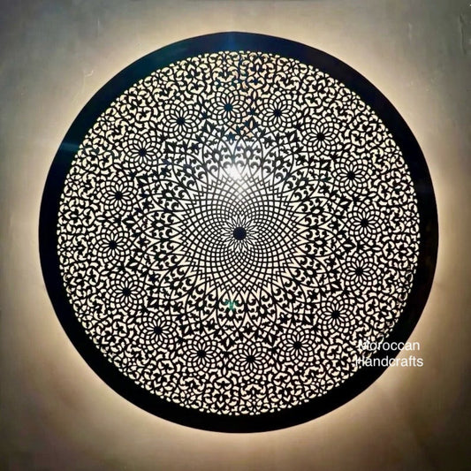 Handmade Moroccan brass wall sconce with geometric piercing pattern, casting a warm ambient light on a textured wall.