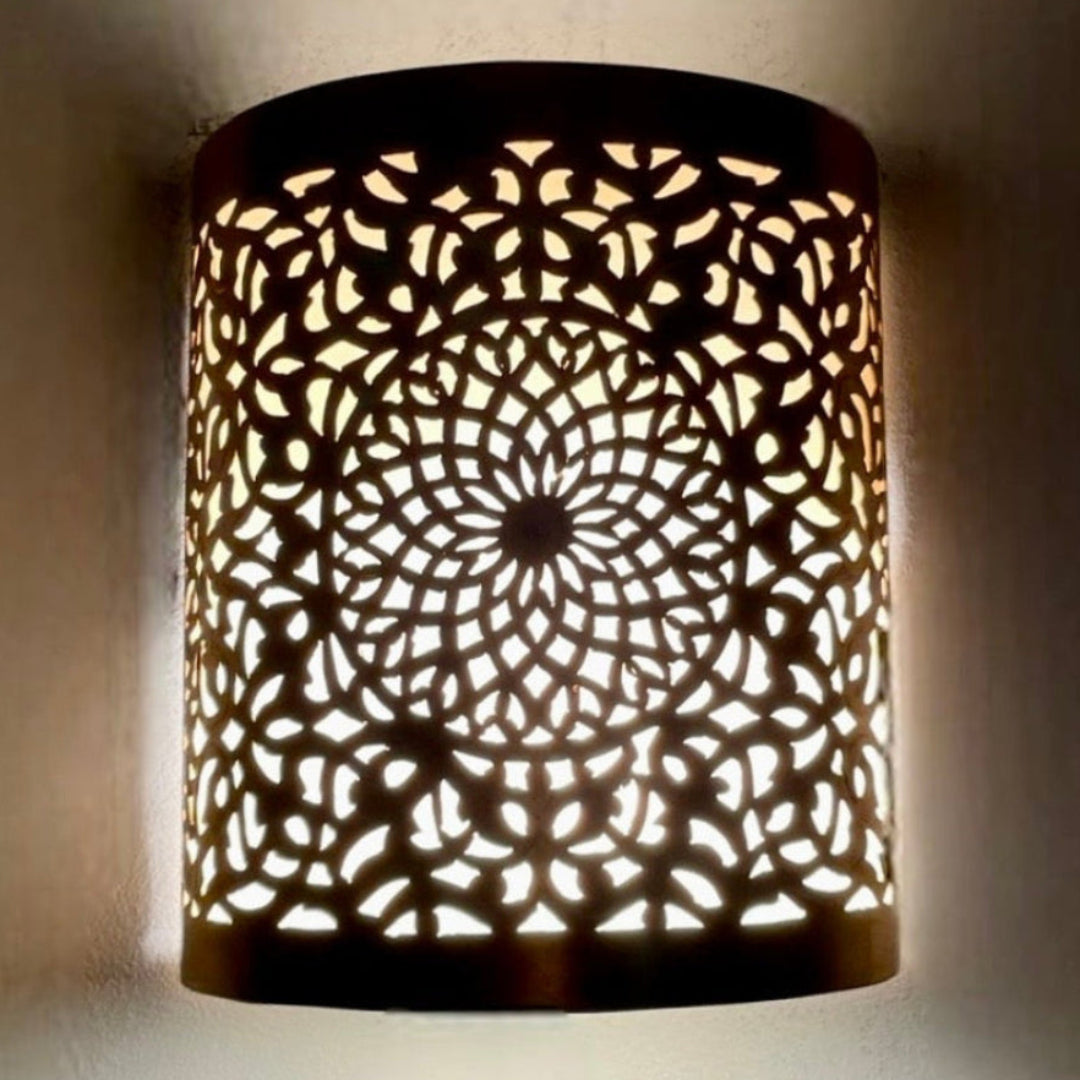 Wall mounted handmade brass Moroccan sconce casting intricate light patterns.