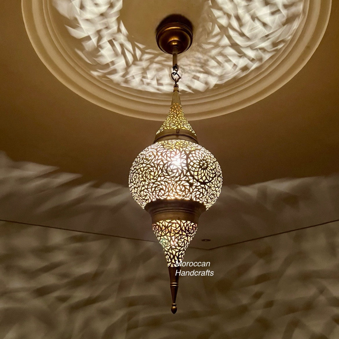 Artisanal brass lamp, teardrop-shaped, projecting mesmerizing wave-like shadows onto the pale interior surfaces.