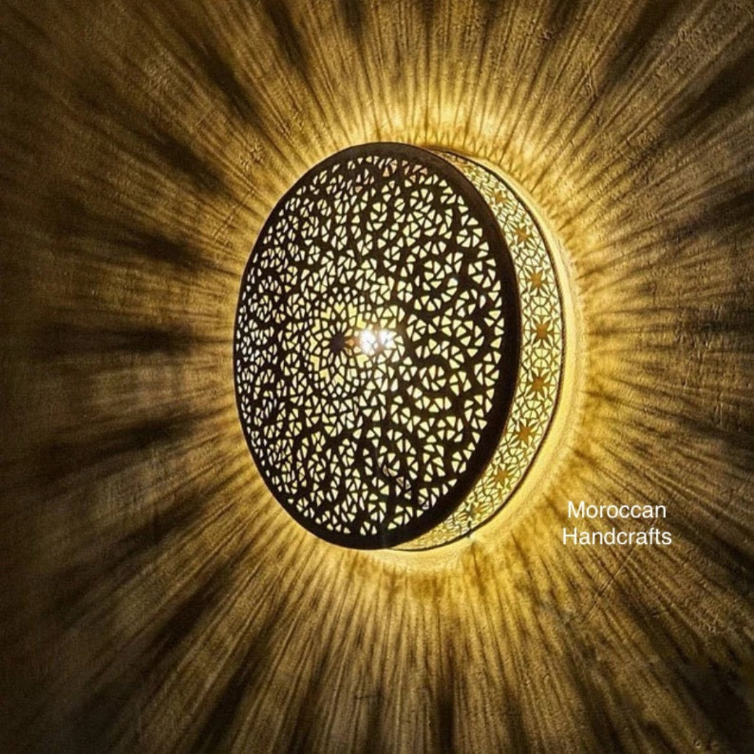 Handcrafted Moroccan brass wall sconce with intricate geometric filigree pattern, casting a warm sunburst shadow.