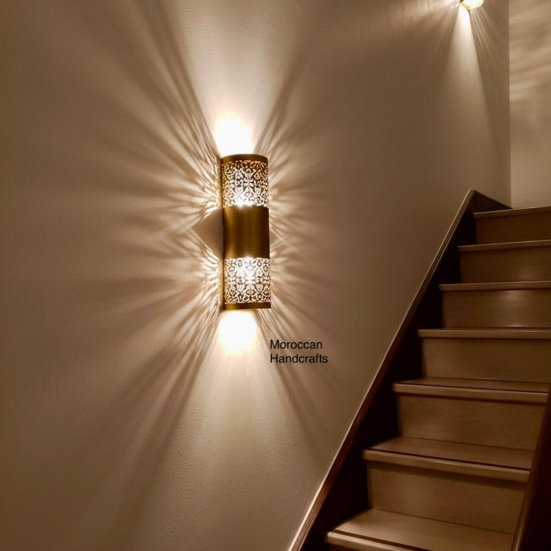 Modern Moroccan brass wall lamp with intricate floral perforations casting a dramatic symmetrical starburst shadow on a hallway wall.