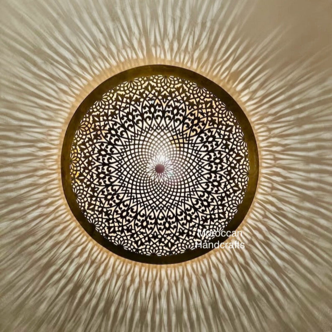 Round Moroccan brass wall sconce casting intricate arabesque shadow patterns on the wall.