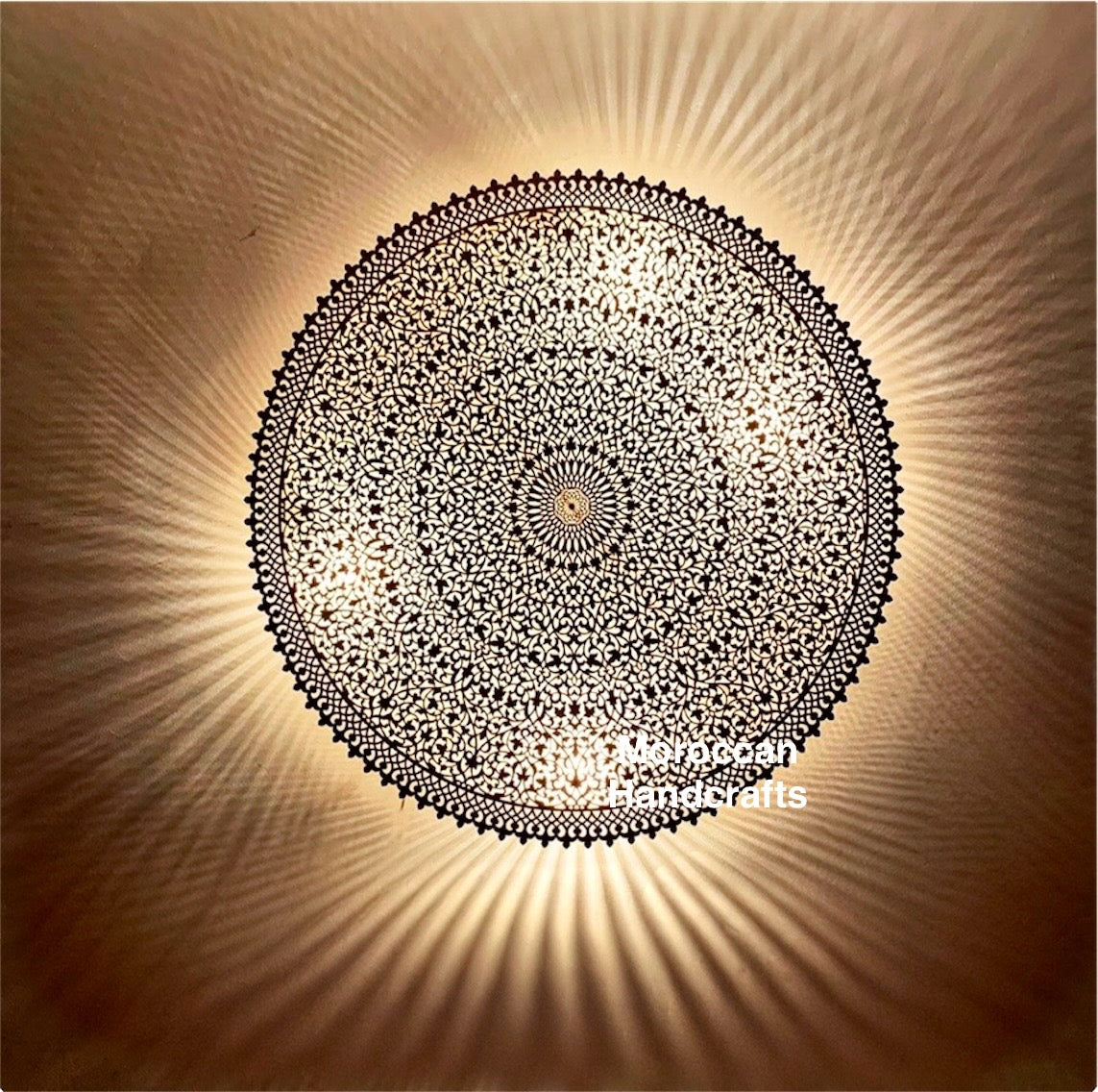 Hand-perforated Moroccan brass flush mount ceiling light casting a mesmerizing radial shadow pattern on a beige wall. Intricate Islamic geometric design.