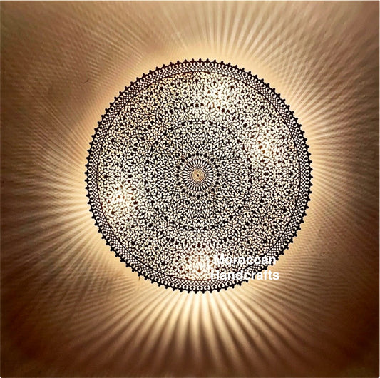 Hand-perforated Moroccan brass flush mount ceiling light casting a mesmerizing radial shadow pattern on a beige wall. Intricate Islamic geometric design.