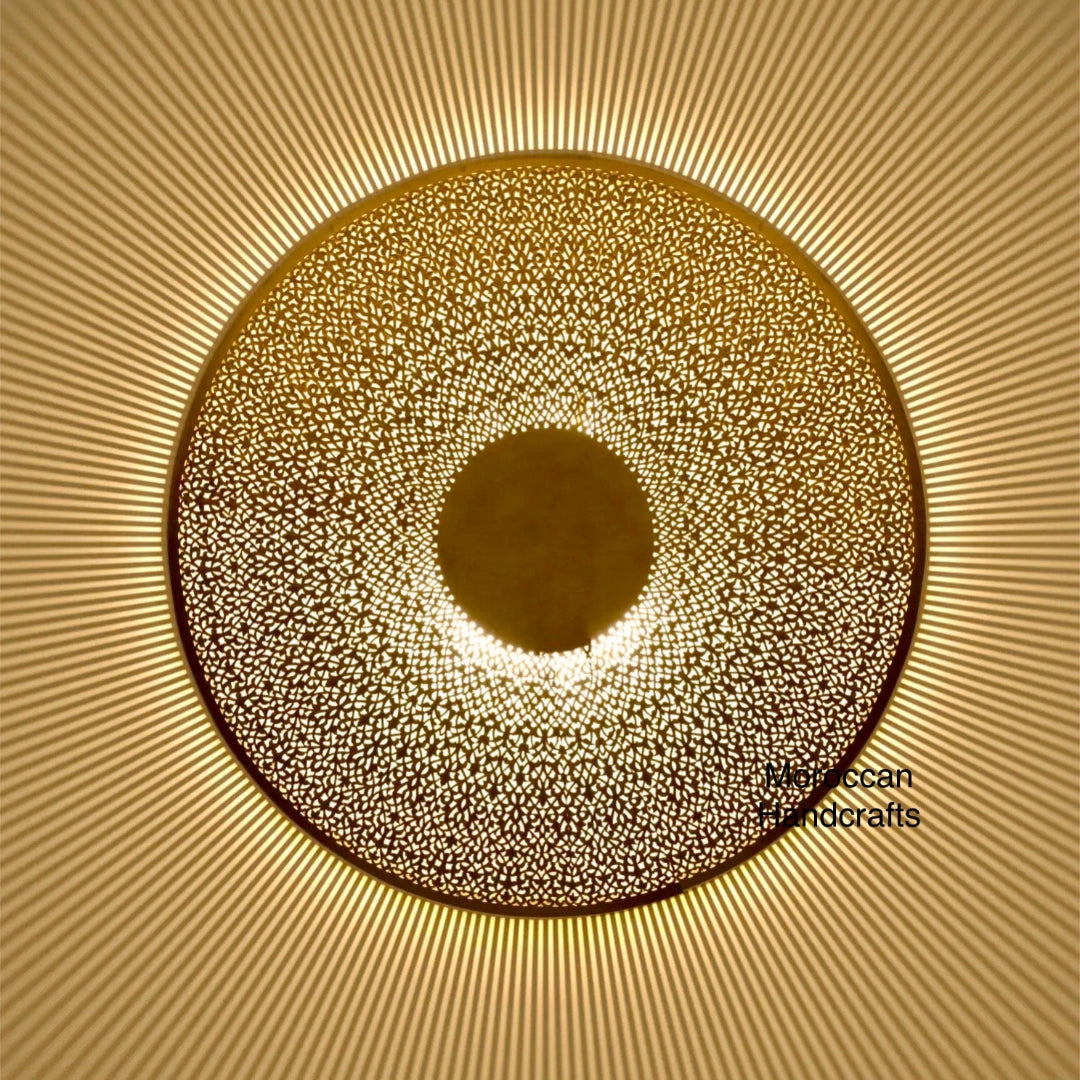 Hand-pierced Moroccan brass flush mount lamp with central solid disc, casting dramatic sunburst radial shadow patterns.