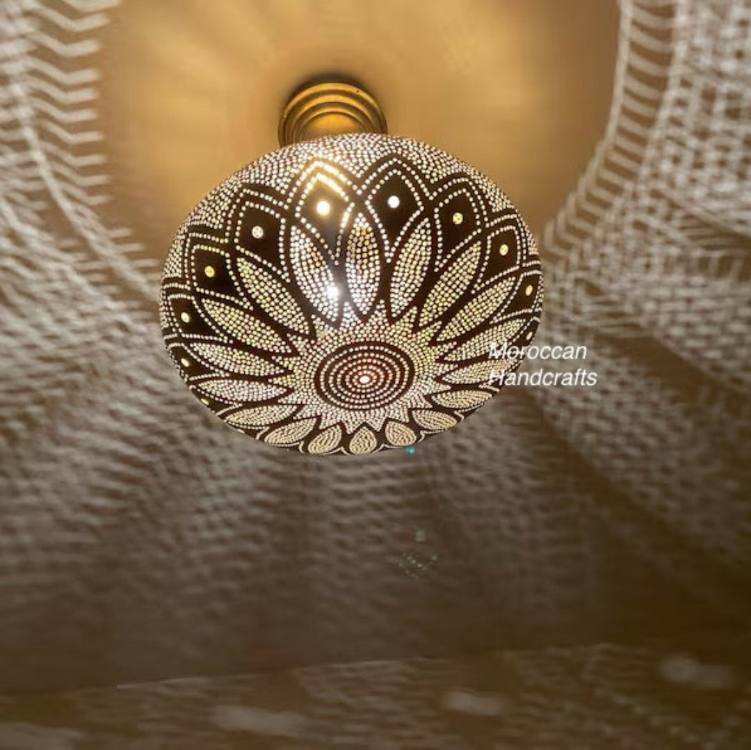 Small oval Moroccan table lamp made of carved brass with a round base, projecting magical light patterns onto the fabric.