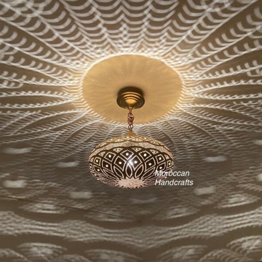 Spherical Moroccan brass pendant light hanging from the ceiling, featuring detailed piercing and projecting an intricate radial pattern on the ceiling and walls.