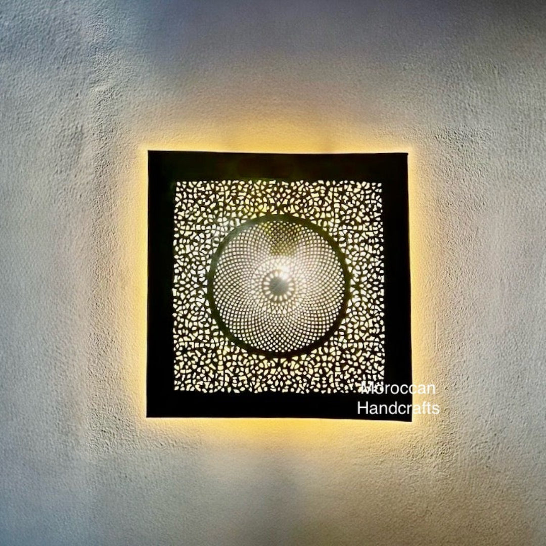 Square Moroccan brass wall sconce with a central circular pattern casting a soft light glow.