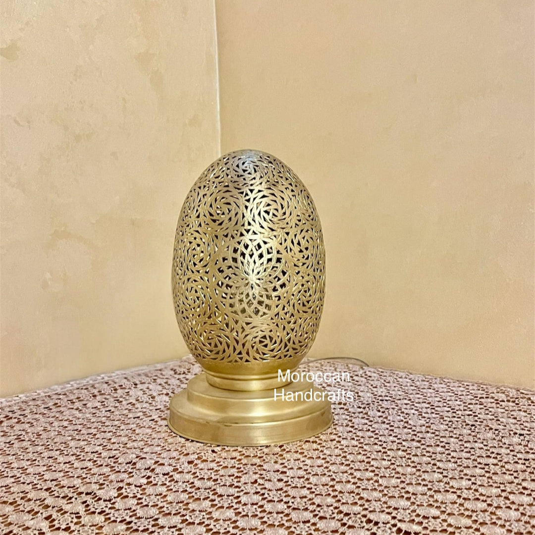 Moroccan brass egg-shaped table lamp with intricate filigree carvings, beautifully casting a complex, detailed shadow pattern onto the wall and surrounding surface.