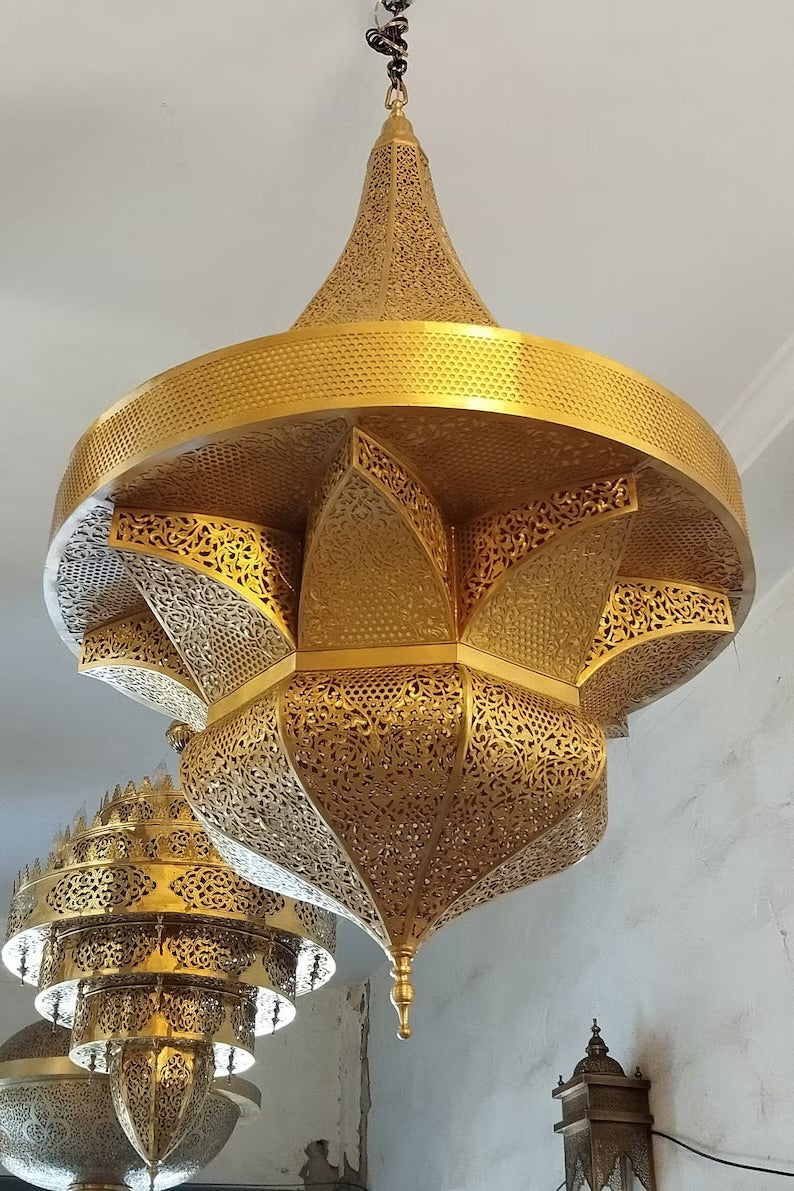 Traditional Moorish pendant light hanging from a dark wood ceiling in a Moroccan riad, featuring authentic filigree metalwork and ethnic design.