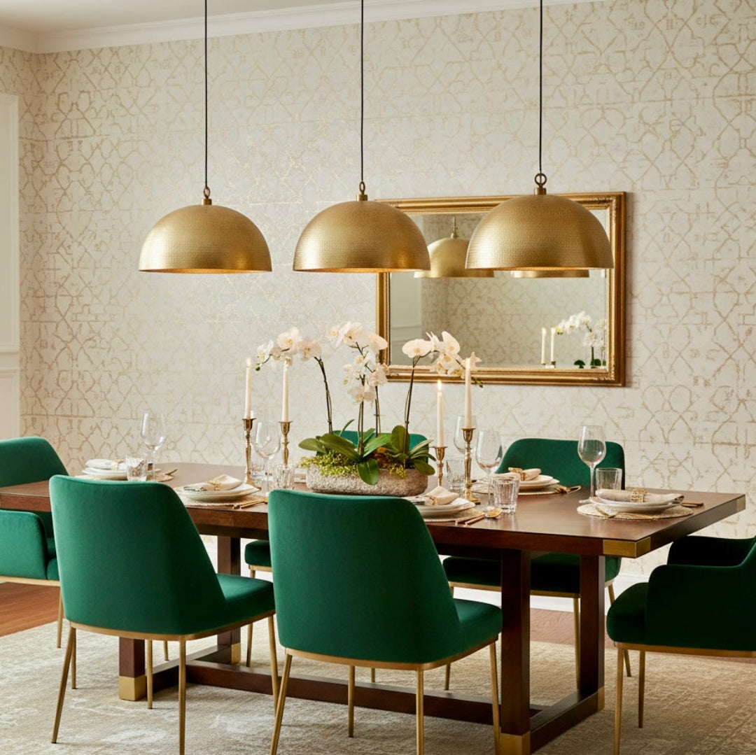 A large single brass dome pendant light hanging above a kitchen island with dark wood cabinets and white calla lilies.