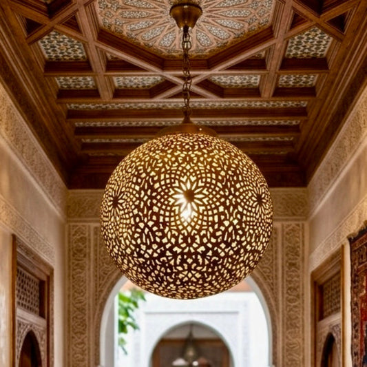 Large spherical Moroccan brass pendant light hanging in a traditional riad hallway with carved wood ceilings and red rugs.