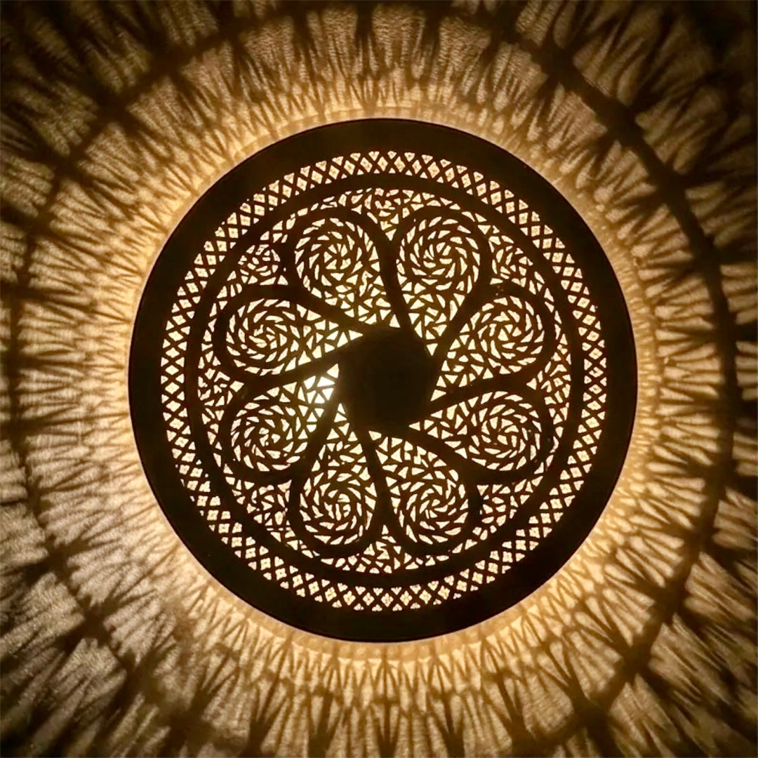  Close-up top view of an illuminated round Moroccan brass ceiling light, showing the detailed artisan craftsmanship and fine geometric fretwork.