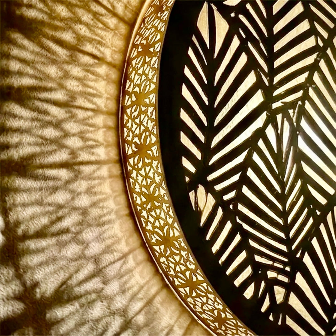 Side view of an illuminated round Moroccan brass wall light fixture, highlighting the golden metallic finish and dramatic radiant shadow projections.