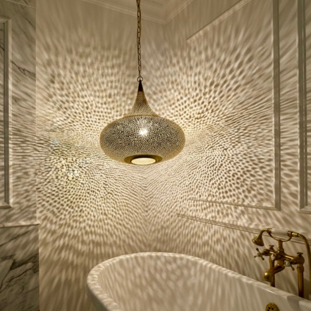 Handmade Moroccan brass lamp illuminating a marble bathroom with decorative light shadows, boho-chic home spa lighting.