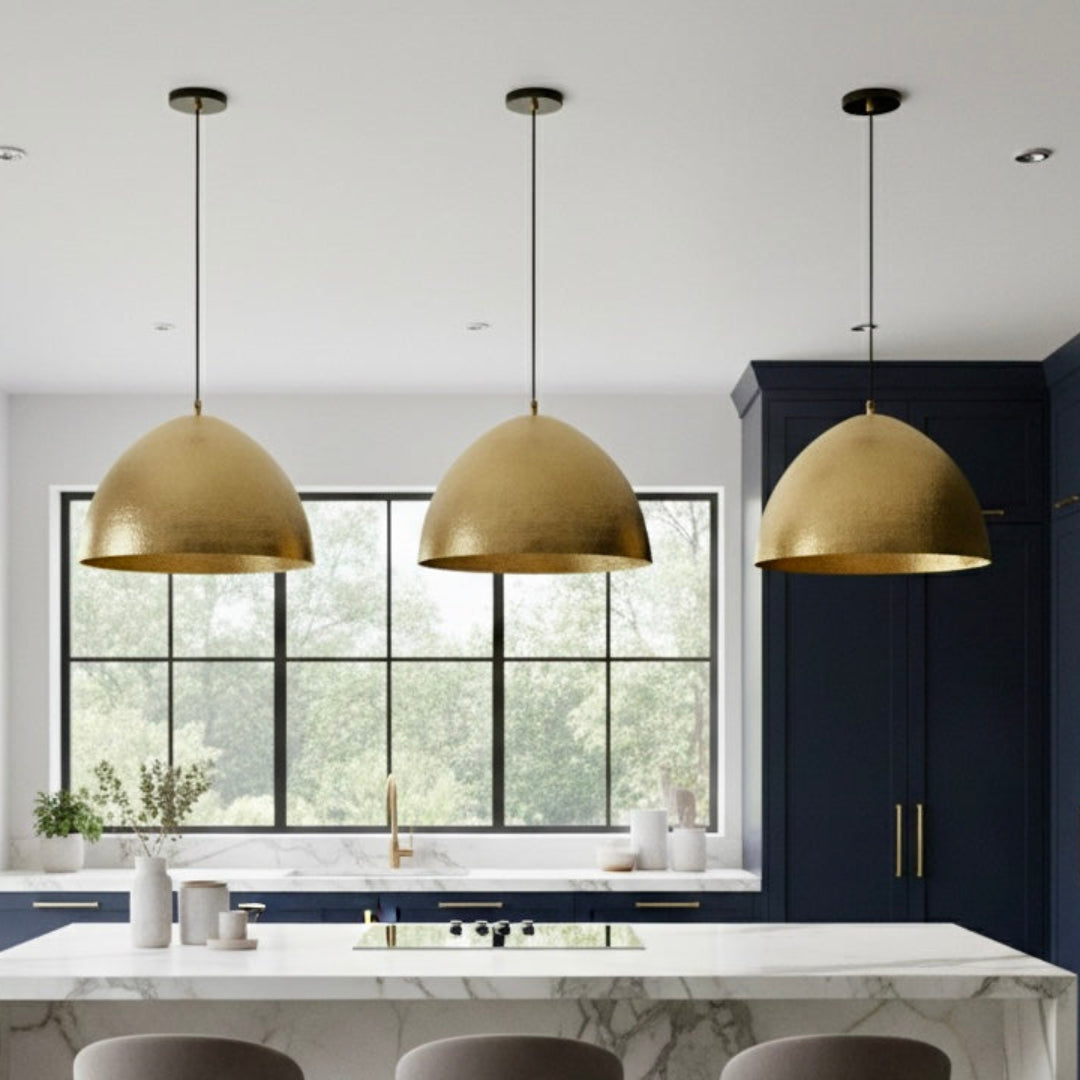 Three brass dome pendant lights installed over a white marble kitchen island with navy blue cabinets.