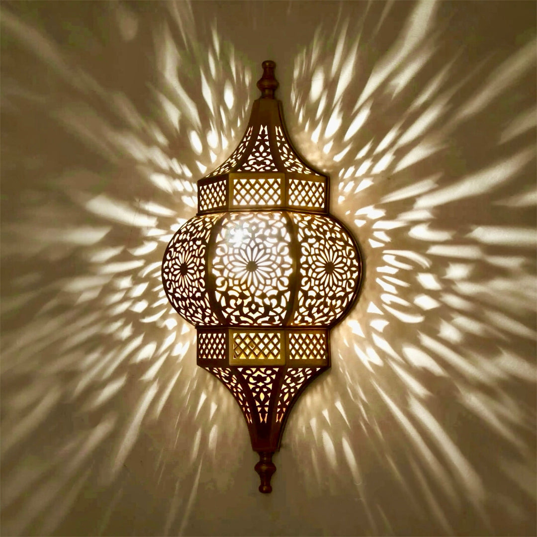 Close-up of a brass wall sconce illuminated, showing the sharp and dramatic ambient shadow projections on a neutral wall.