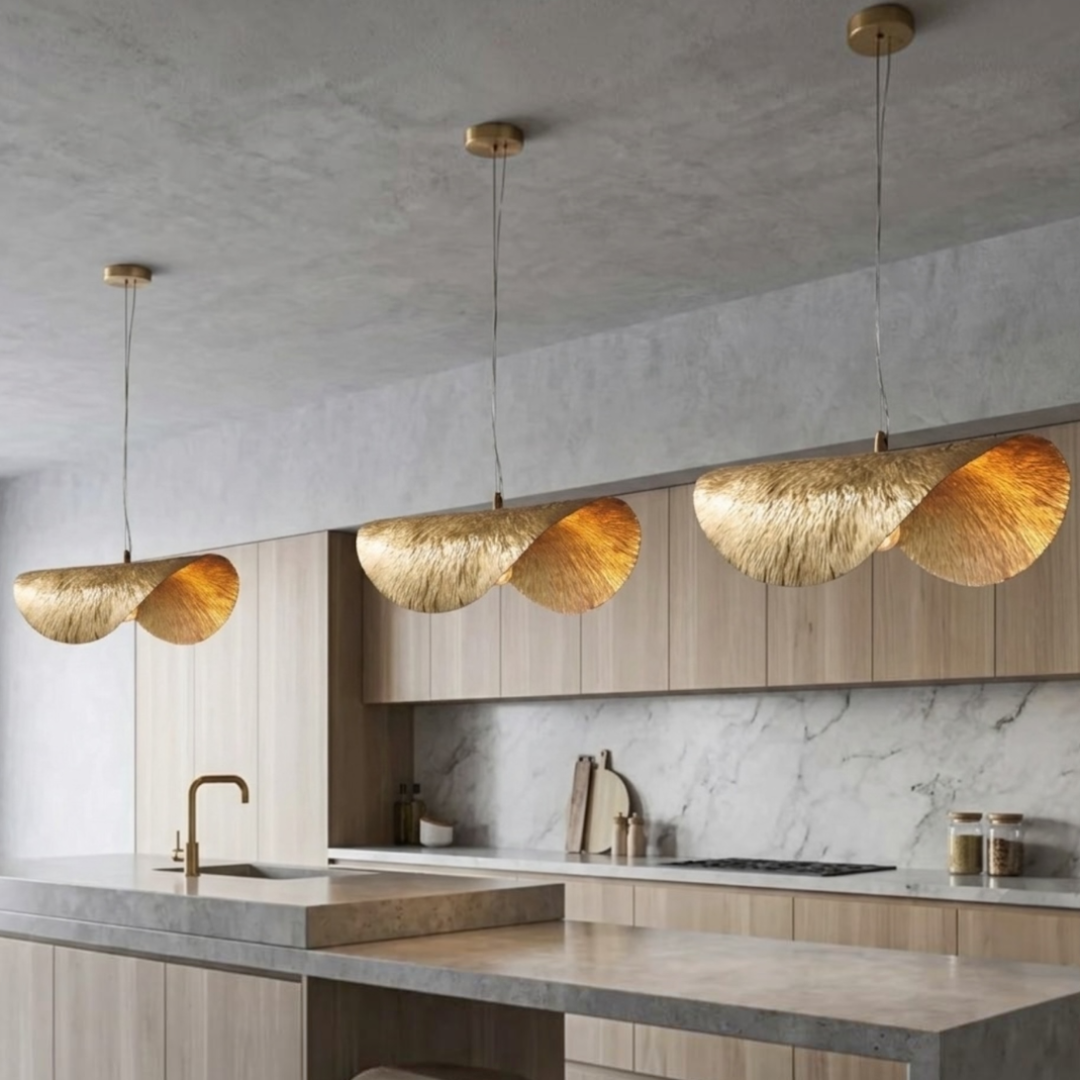 Trio of warm illuminated Moroccan brass wave pendant lights over a light wood kitchen island and marble countertop