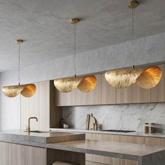 Trio of warm illuminated Moroccan brass wave pendant lights over a light wood kitchen island and marble countertop