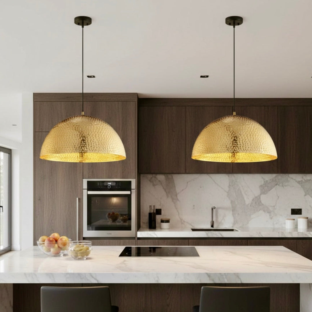 Two contemporary brass dome pendant lights with black cords installed over a marble kitchen island in a modern dark wood kitchen.