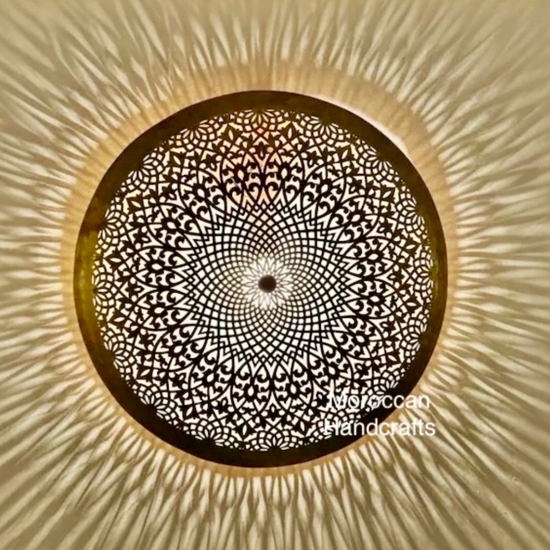 Overhead view of an illuminated round Moroccan flush mount brass lamp with fine floral geometric patterns, creating a beautiful warm glow and expansive ambient shadow art.