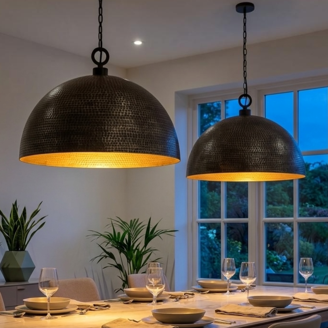  Pair of modern hammered brass dome pendant lights emitting warm gold light over a stylish contemporary dining set