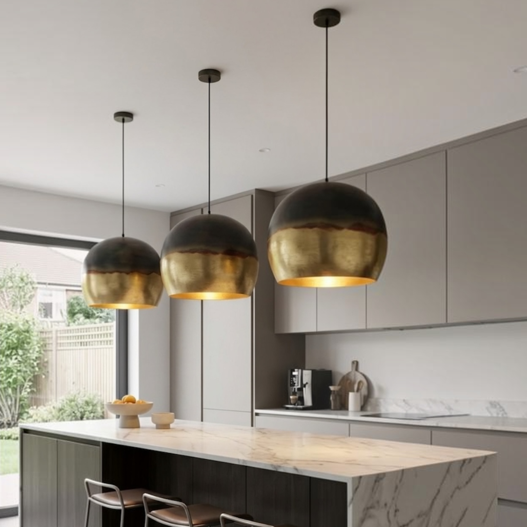 Trio of modern Moroccan brass dome pendant lights mounted over a white marble kitchen island in a minimalist modern space