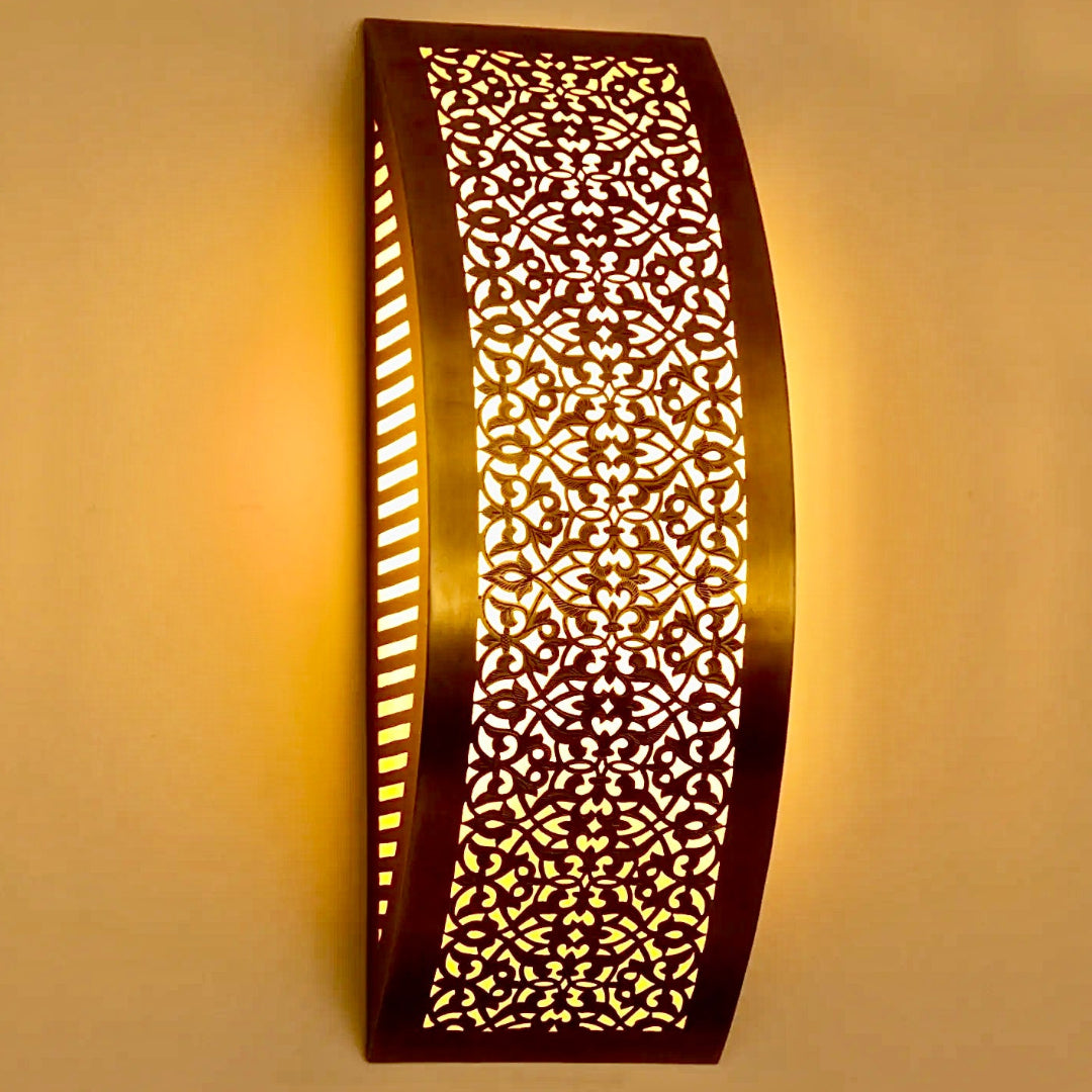 Side view of a curved Moroccan brass wall sconce with intricate floral carvings casting a warm glow.