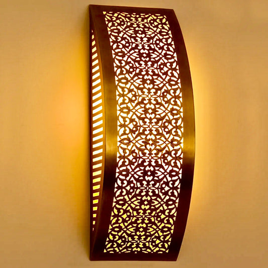 Side view of a curved Moroccan brass wall sconce with intricate floral carvings casting a warm glow.