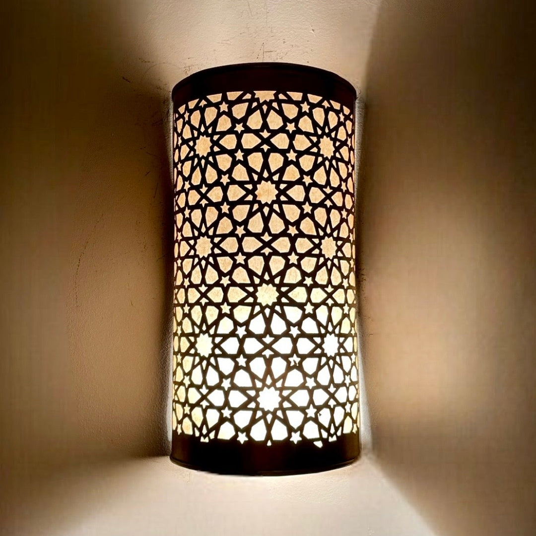  Close-up of a handmade cylindrical brass wall sconce showing intricate hand-drilled geometric star patterns.