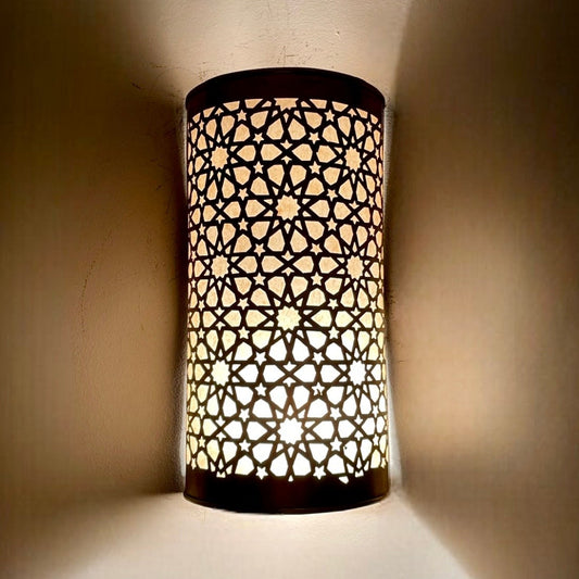 Close-up of a handmade cylindrical brass wall sconce showing intricate hand-drilled geometric star patterns.