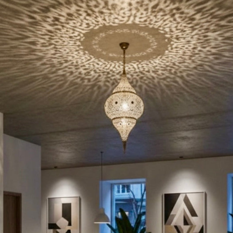 Warm ambient lighting in a restaurant featuring a Moroccan filigree brass lamp with shadow patterns on white walls.