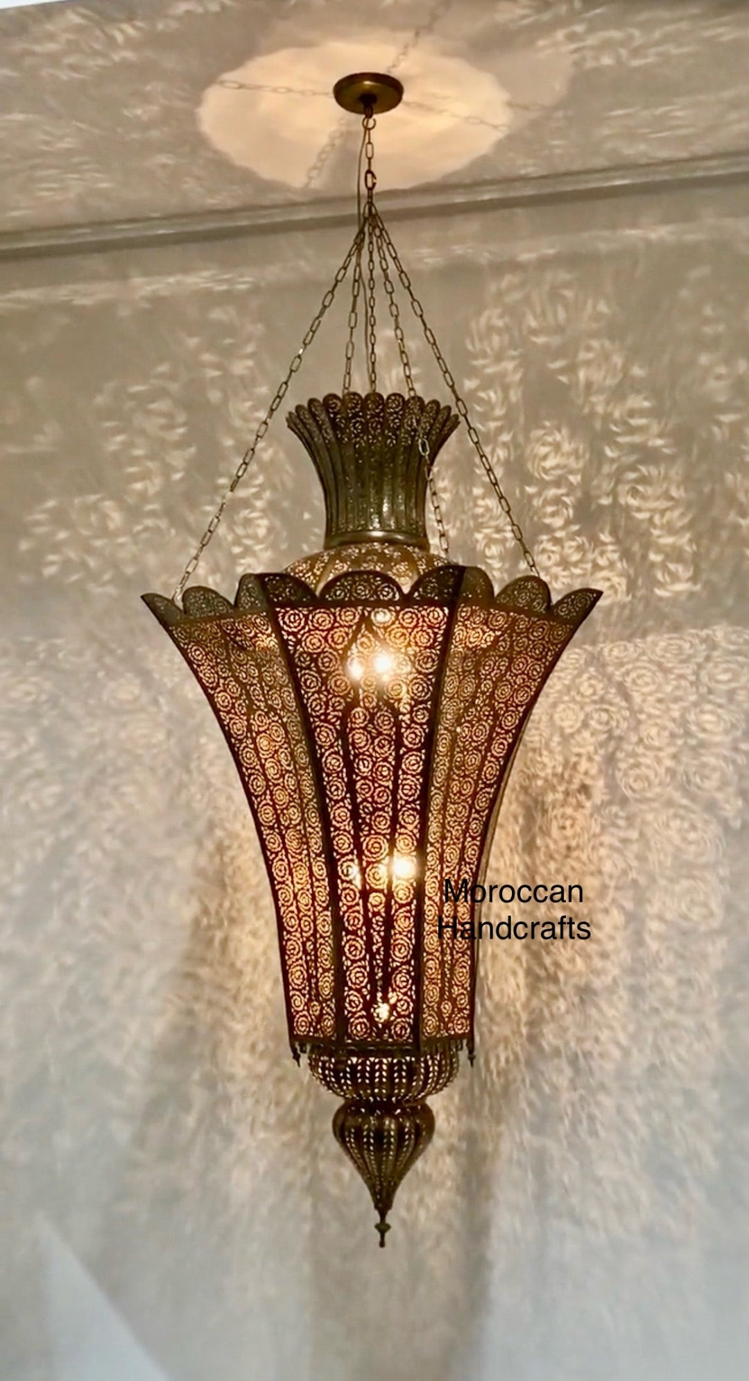 Flared, Moorish suspension lamp with intricate reticulated metalwork, casting swirling shadow-casting patterns.