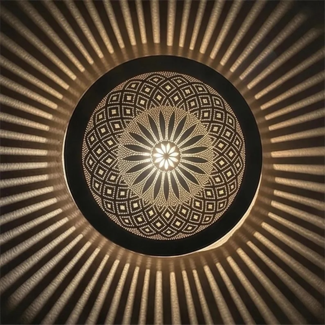 Symmetrical frontal view of a round Moroccan brass filigree ceiling lamp lit up, displaying a central floral motif and a starburst of warm light rays on the ceiling.