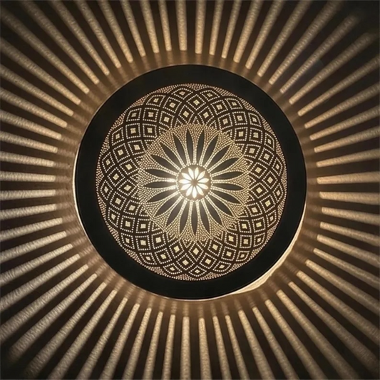 Symmetrical frontal view of a round Moroccan brass filigree ceiling lamp lit up, displaying a central floral motif and a starburst of warm light rays on the ceiling.