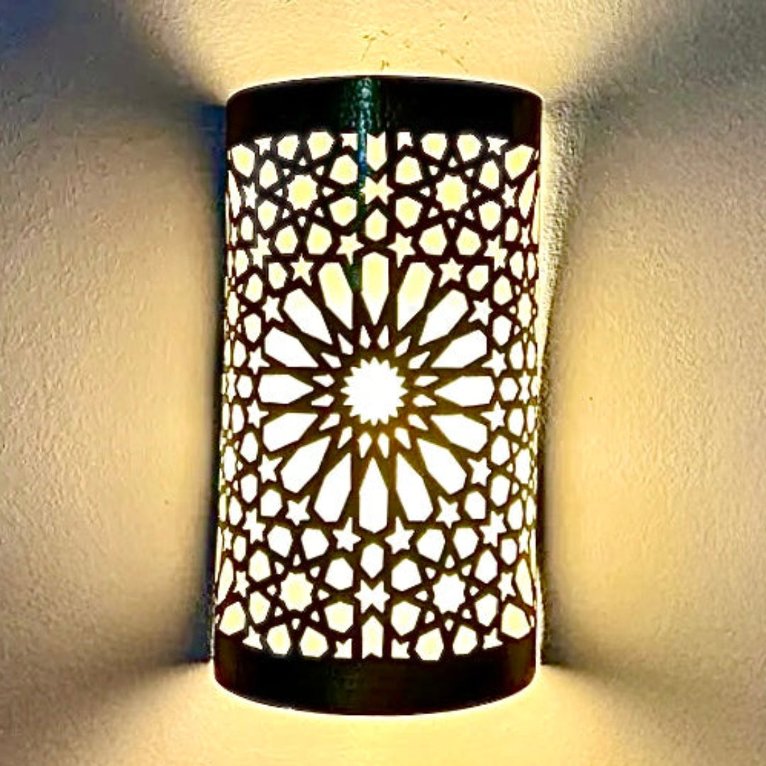 Close-up of a handcrafted Moroccan brass wall lamp featuring intricate geometric star patterns with warm light glowing through the cutouts.