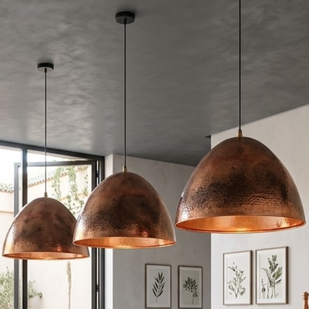 Three handcrafted Moroccan brass dome pendant lights with warm red-copper patina installed over a sleek kitchen island