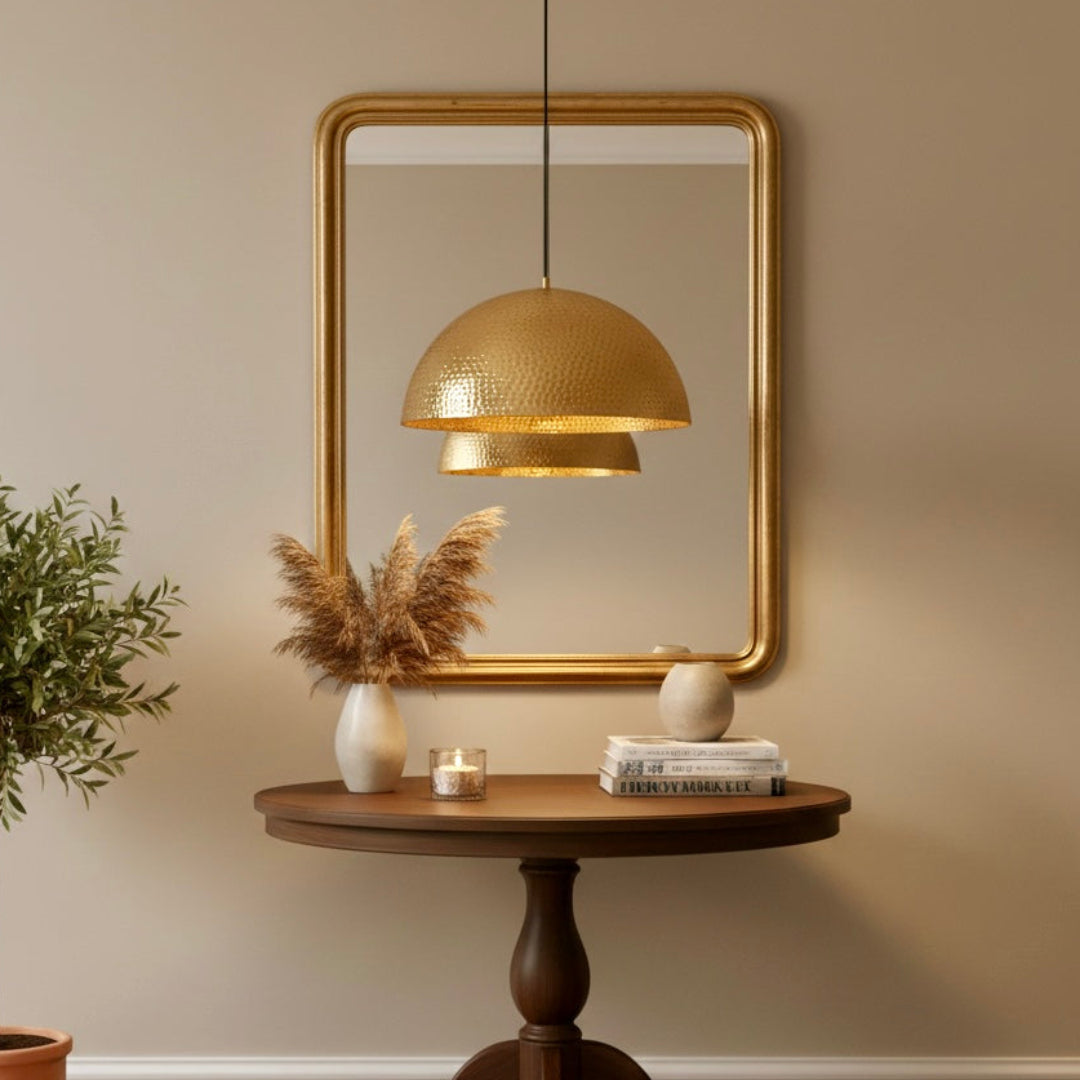 Handmade Moroccan brass dome lamp reflecting in a gold-framed mirror above a wooden foyer console table.